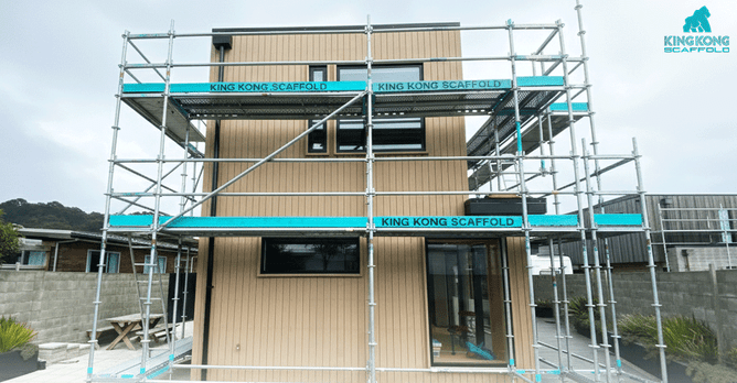 Aluminum scaffolding with multiple safety platforms erected around a modern, two-story home with vertical timber cladding.