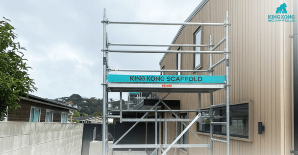 Close-up of modular aluminum scaffolding set up next to the exterior of a residential house with tan siding, ready for construction or maintenance work.