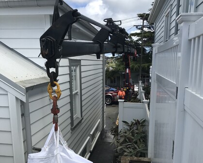 Photo of a hiab crane arm carefully moving item between two houses