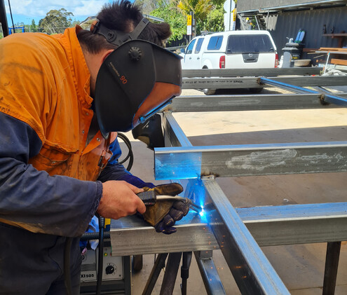 Mackenzie Transport engineer wearing welding helmet, welding a metal truck trailer component