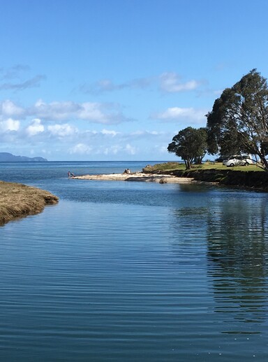 The Kuaotunu rivermouth with a family sitting on the sand looking at Great Mercury Island in the distance 