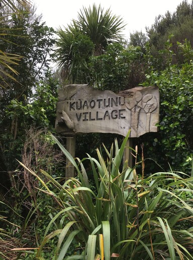The wooden Kuaotunu Village sign nestled in native bush at the entrance to Kuaotunu on the Coromandel Peninsula