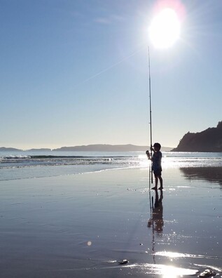 A boy standing with his fishing rod in the late evening sun at Kuaotunu Beach on the Coromandel Peninsula