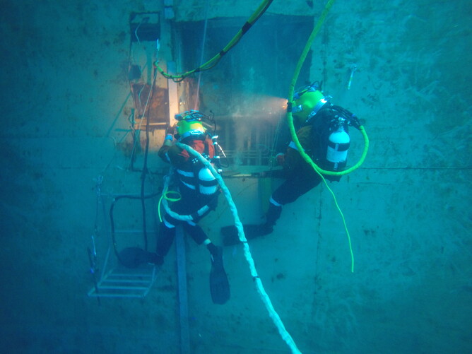 Two commercial divers working underwater on a submerged structure with safety lines and equipment.