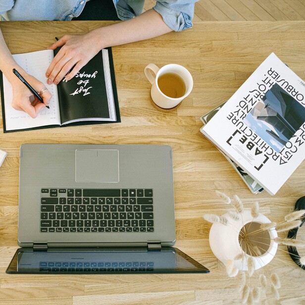 Laptop on desk with books and vase with stems. Virtual Office Manager writing in a diary.