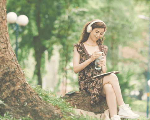 A person sitting under an established tree looking peaceful and relaxed as they listen to beautiful music through headphones. This represents listening to the music of the Tomatis method completely relaxed and peaceful.