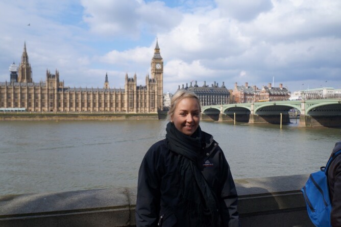 Holly on one side of the Thames River with Big Ben, the Houses of Parliament and the Westminster bridge in the background.