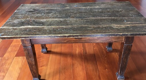 A medium-sized old kauri table standing on the wooden floor of the Kūaotunu Hall