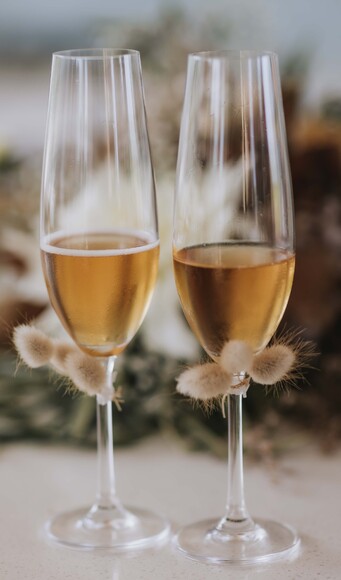 A pair of champagne glasses decorated with catkins sitting on a table at a wedding reception at the Kūaotunu Hall