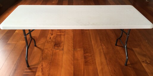 A plastic-topped trestle table standing on the wooden floor of the Kūaotunu Hall