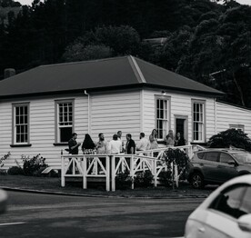 A black and white photo of a wedding party standing on the ramp outside the Kūaotunu Hall