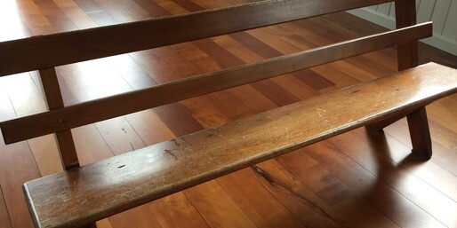 An old kauri pew standing on the wooden floor of the Kūaotunu Hall