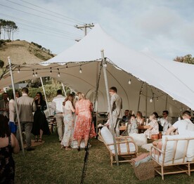 A wedding reception being held in a marquee on the back lawn of the Kūaotunu Hall