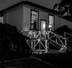 A black and white photo showing the exterior of the Kūaotunu Hall building, including the ramp, lit up for a wedding