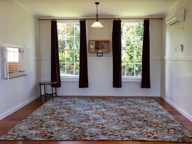 The annex area of the Kūaotunu hall with a floral axminster carpet on the floor and sash windows on the far wall