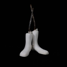 A pair of white boot/feet shapes made of plaster. Each with a nylon stocking sheath stretched over it and knotted at the top where a steel reinforcing rod protrudes out of the boot shape. These boot shaped plaster objects stand as a pair on a square black back ground.