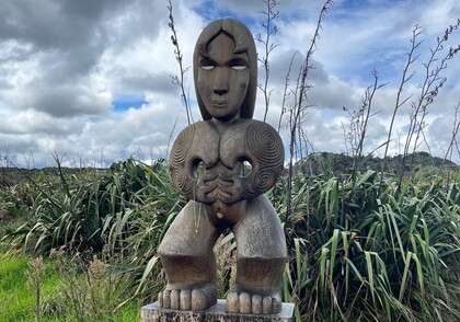 Maori Pou carving in front of flax bushes
