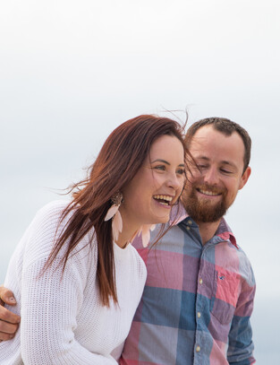 Couple laugh together as they walk down the beach