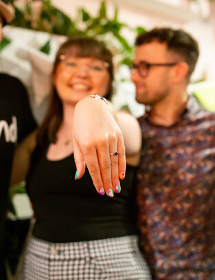 Women poses next to her Fiancee, her hand outstretched showing off her new ring