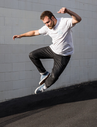 Man poses by jumping In the air and clapping his feet together in industrial car park photoshoot