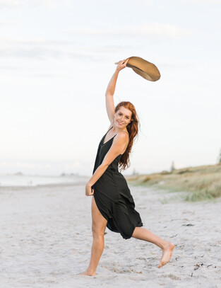 Girl poses on beach holding her hat in the air
