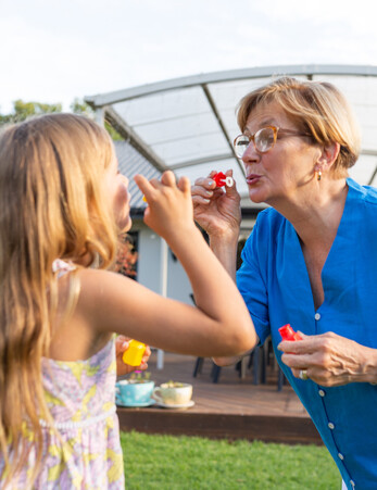 Grandmother blows bubbles to her young granddaughter